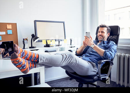 Entspannt Mann sitzt am Schreibtisch im Büro mit Handy Stockfoto