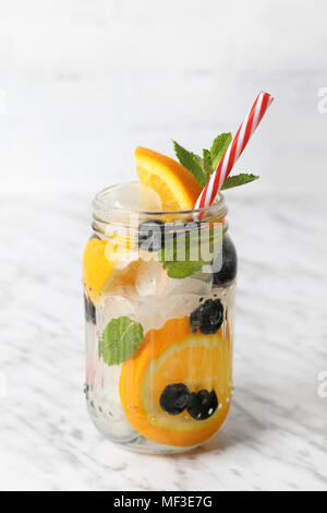 Glas infundiert Wasser mit Orange, Blaubeeren und Minze auf Eis Stockfoto