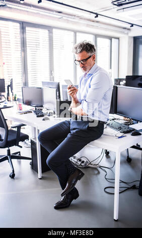 Reife Unternehmer sitzen am Schreibtisch im Büro mit Smartphone Stockfoto