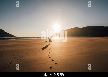 Kanada, Britisch-Kolumbien, Vancouver Island, zwei Männer zu Fuß am Strand von San Josef Bucht bei Sonnenuntergang Stockfoto