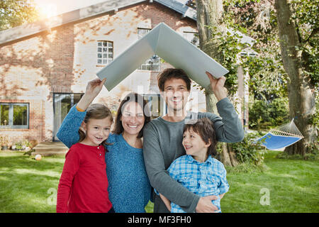 Portrait von Happy Family im Garten ihres Hauses holding Dach Stockfoto