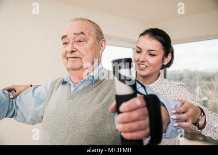 Junge Frau die Unterstützung älterer Mann, der eine Arm Übung Stockfoto
