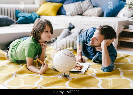 Vater und Sohn essen Pizza neben der Kugel auf dem Boden zu Hause Stockfoto