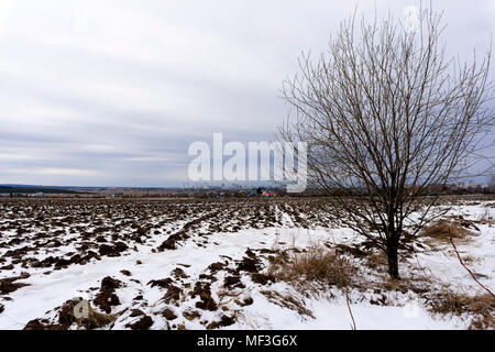 Feld mit der Schneeschmelze im Frühjahr gepflügt, mit einem Dorf in der Ferne und eine Stadt am Horizont Stockfoto