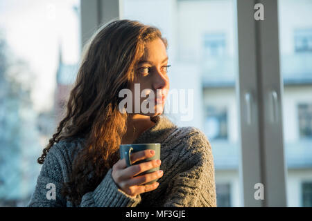 Portrait von jugendlichen Mädchen mit kaffeebecher Blick aus Fenster am Abend Stockfoto