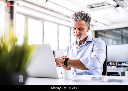 Reifen Geschäftsmann am Schreibtisch im Büro an smartwatch suchen Stockfoto