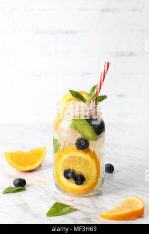 Glas infundiert Wasser mit Orange, Blaubeeren und Minze auf Eis Stockfoto