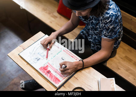 Künstler sitzen im Cafe, Zeichnung in seinem Notebook Stockfoto