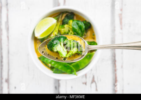 Green Thai curry mit Broccoli, Pak Choi, Zuckerschoten, Baby Spinat, Kalk, Brokkoli und Sauce auf Löffel Stockfoto