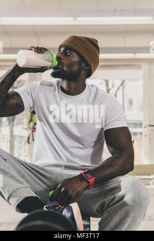 Mann sitzt auf der Bank in der Turnhalle das Trinken aus der Flasche Stockfoto