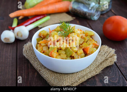 Vegetarische Ragout von Sommer Gemüse (Zucchini, Karotten, Tomaten, Gewürze, Knoblauch, Chili) in einer weißen Schüssel auf einem hölzernen Hintergrund. Diätetische Gerichte. Stockfoto