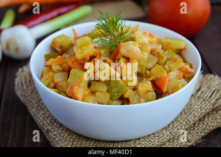 Vegetarische Ragout von Sommer Gemüse (Zucchini, Karotten, Tomaten, Gewürze, Knoblauch, Chili) in einer weißen Schüssel auf einem hölzernen Hintergrund. Diätetische Gerichte. Stockfoto