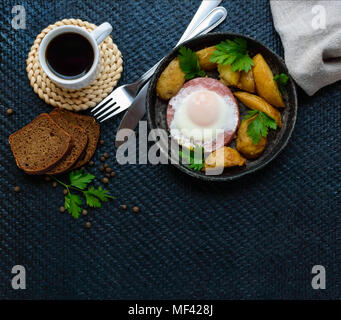 Spiegelei in Salami und gebackene Kartoffeln. Einreichung von eine Pfanne mit einer Tasse Kaffee und Roggenbrot. Frühstück. Die Ansicht von oben Stockfoto