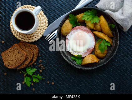 Spiegelei in Salami und gebackene Kartoffeln. Einreichung von eine Pfanne mit einer Tasse Kaffee und Roggenbrot. Frühstück. Die Ansicht von oben Stockfoto