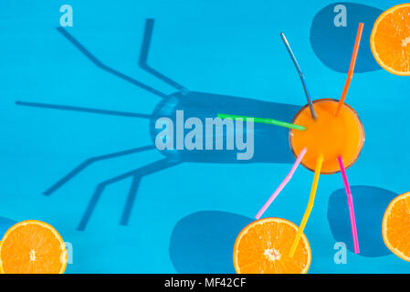 Fröhliches Bild von oben mit einem Glas frisch gepressten Orangensaft mit Strohhalm und orange Hälften auf einem blauen Hintergrund, in natürliches Licht und Schatten. Stockfoto
