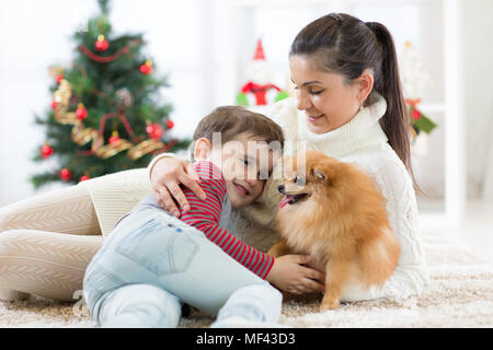 Familie Mutter und Sohn spielen mit Hund am Weihnachtsbaum Stockfoto