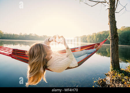 Junge Frau entspannen auf der Hängematte, die Form eines Herzens finger Rahmen auf dem wunderschönen See Landschaft, Menschen lieben Romantik Konzept. Frankreich, Europa Stockfoto