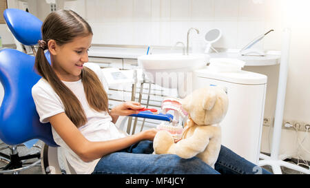 Süß lächelnde Mädchen spielen in Zahnarzt und Patient mit ihrem Teddybär Stockfoto