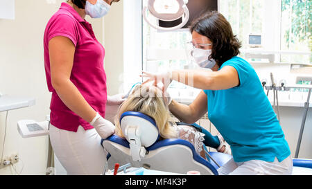 Zahnarzt in portective Maske und Brille treting Patientin Stuhl Stockfoto