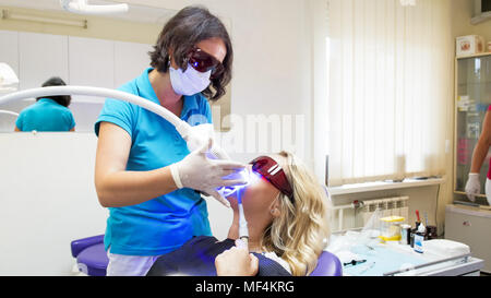 Weibliche Zahnarzt in schützende orange brille Anpassen der UV-Lampe für Zähne, die Stockfoto