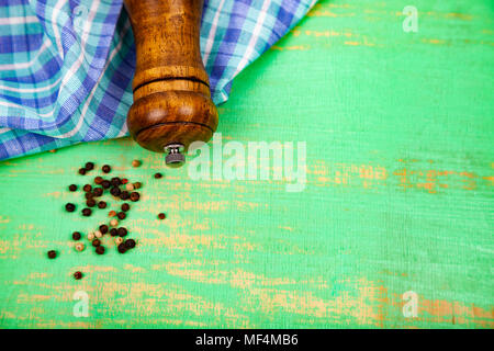 Pfefferkörner, Pfeffer Mühle und ein Handtuch auf ein grünes Holz- Hintergrund. Stockfoto
