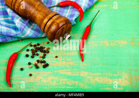 Mühle Pfefferkörner, Pfeffer, Chili und ein Handtuch auf ein grünes Holz- Hintergrund. Stockfoto