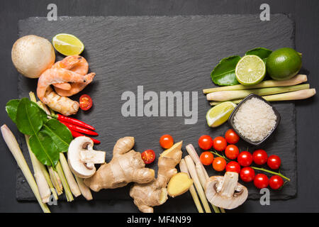 Spezielle Zutaten für populäre thailändische würzige Suppe Tom - Yum Kung Kalk, Galgant, roter Chili, Cherry Tomaten, Zitronengras und Kaffernlimette Blatt auf Schwarzen Tisch Stockfoto