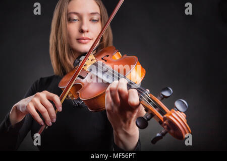 Schöne junge Frau spielt die Geige auf dunklem Hintergrund Stockfoto