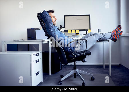 Mann an Schreibtisch im Büro entspannend Stockfoto
