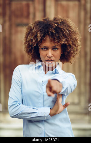 Spanien, Andalusien, Malaga. Junge schwarze Frau, afro Frisur und zeigt mit dem Finger auf der Straße. Mädchen, Modell von Mode, legere Kleidung in Stockfoto