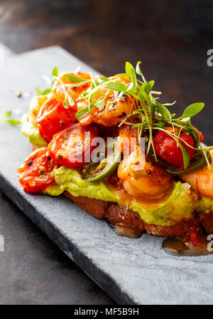 Crostini mit Garnelen und Tomaten, geröstete Brot, Kräuter, Avocadocreme, Sweet Chili Sauce, Jalapenos, Kresse Stockfoto