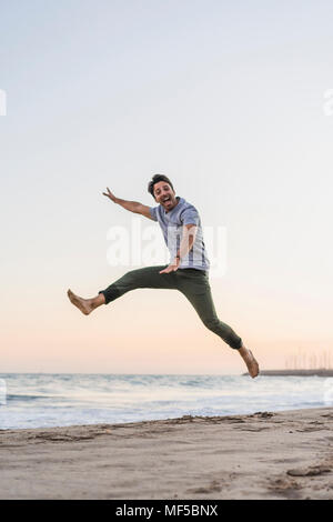 Glückliche junge Mann springen in die Luft am Strand bei Sonnenuntergang Stockfoto