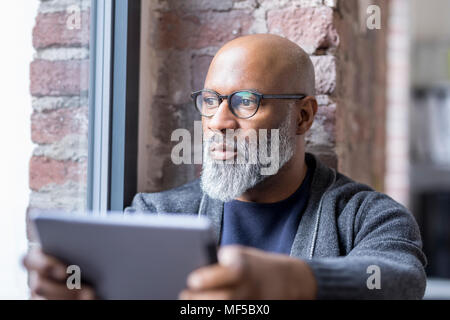 Portrait von nachdenklicher Mann mit Tablet Blick aus Fenster Stockfoto