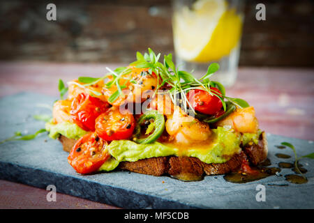 Crostini mit Garnelen und Tomaten, geröstete Brot, Kräuter, Avocadocreme, Sweet Chili Sauce, Jalapenos, Kresse Stockfoto