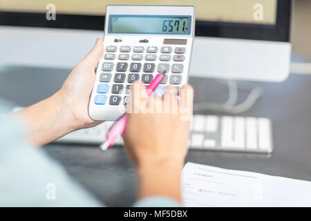 Frau am Schreibtisch im Büro mit Taschenrechner Stockfoto