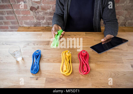 Geschäftsmann mit Tablet Auswahl aus farbigen Netzkabel von Table Top, Teilansicht Stockfoto