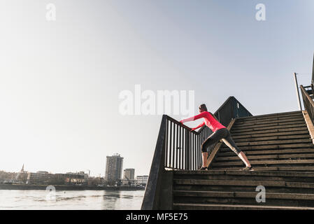 Junge Frau, die sich auf der Treppe an einem Fluss in der Stadt Stockfoto