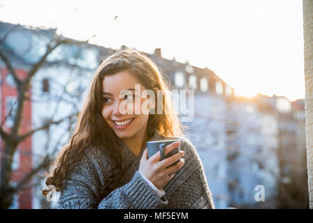 Portrait von Lachen Jugendmädchen mit Kaffeetasse auf dem Balkon in der Dämmerung Stockfoto