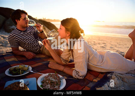 Glückliches Paar bei einem Picknick am Strand bei Sonnenuntergang Stockfoto