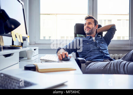 Entspannt Mann sitzt am Schreibtisch im Büro auf dem Bildschirm Stockfoto