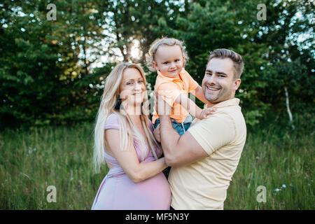 Eine glückliche Familie, die Zeit in der Natur. Das Porträt einer schwangeren Frau und ihrem Partner ihren jungen Sohn umarmen. Stockfoto