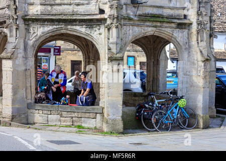 Radfahrer und Besucher nehmen Schutz vor der heißen Sonne auf dem Markt Kreuz, Malmesbury, Wiltshire, Großbritannien Stockfoto