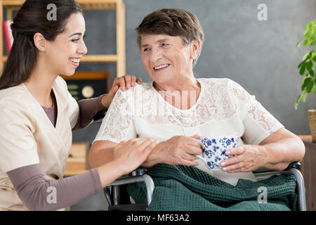 Schöne Betreuer sprechen auf einen Rentner in einem Rollstuhl bei einem Kaffee Stockfoto