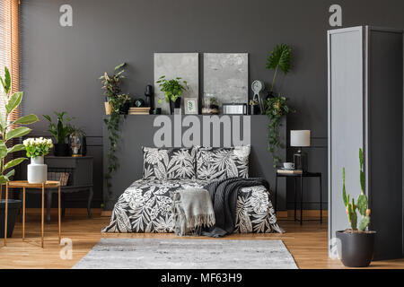 Weiße Rosen und Kakteen in geräumigen grau Schlafzimmer Einrichtung mit gemusterten Laken auf dem Bett Stockfoto