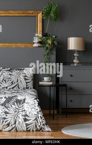 Gold Lampe auf grau Schaltschrank in floralen Schlafzimmer Innenraum mit Mockup von leeren Rahmen Stockfoto