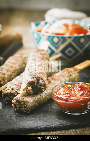 Traditionelle hausgemachte gegrillte Türkischen Adana Urfa Kebap, Hackfleisch Kebab, auf schiefer Teller mit Salat und Soße über Holz- Hintergrund Stockfoto