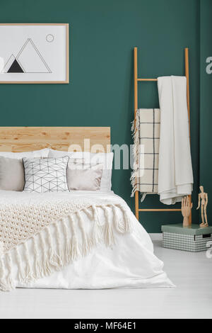 Beige Decken auf dem Bett und Leiter in boho Schlafzimmer Innenraum mit Poster über die grüne Wand Stockfoto