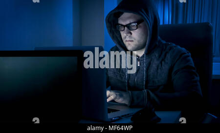 Junge konzentriert Mann in hoodie Arbeiten an latop bei Nacht. Konzept der Internetkriminalität Stockfoto