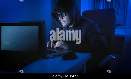 Junger Mann in Brillen hoodie tragen mit Laptop zu Hause. Konzept der Internetkriminalität Stockfoto