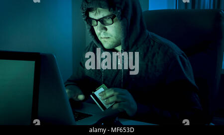 Portrait von konzentriertem Hacker stehlen Geld von Kreditkarten bei Nacht Stockfoto